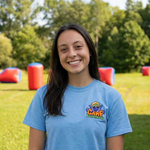 Madi, a Kustermans camp counsellor, smiling in the farm field wearing a Camp Kustermans shirt